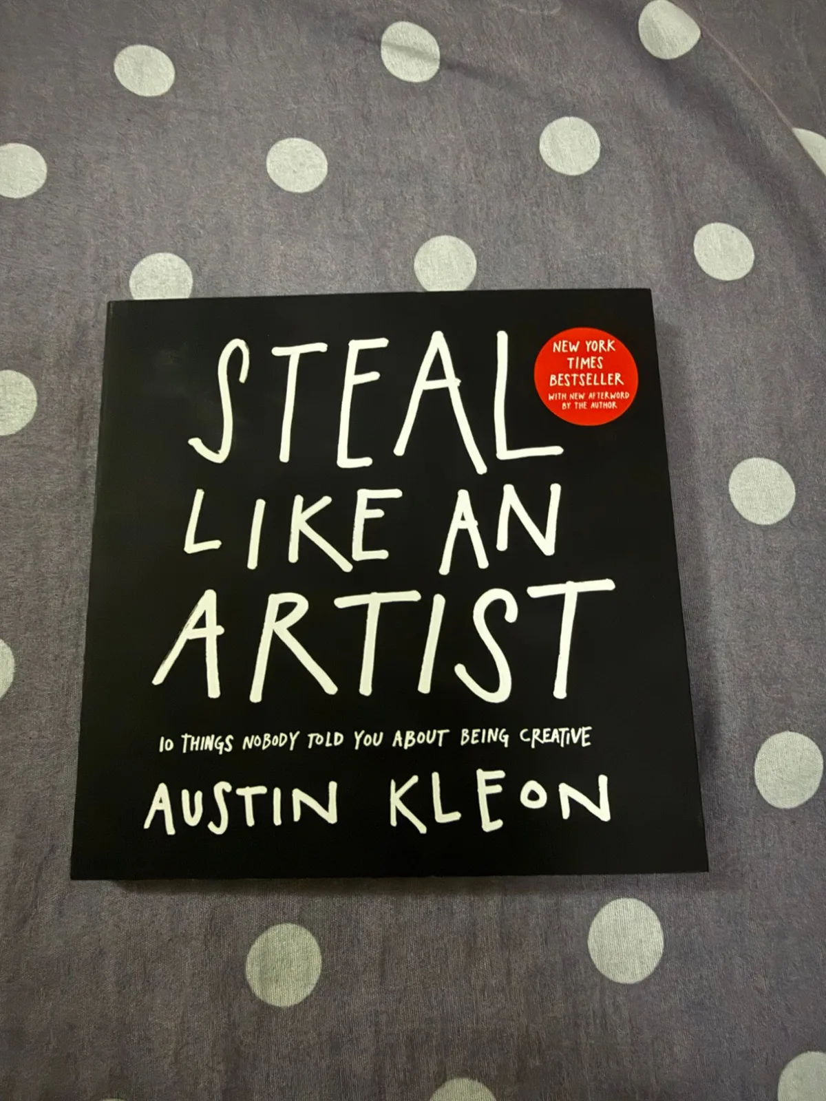 Steal Like an Artist by Austin Kleon, a black paperback with white hand-lettered title, lying on a purple polka-dot bedspread.